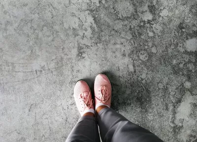 A pair of feet in pink shoes stand on a gray stone slab.