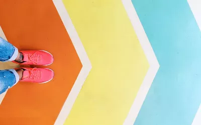 A pair of feet in pink sneakers stand on a colored path of chevron arrows.