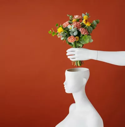 a bouquet of red and yellow flowers is placed into a vase shaped like a head.