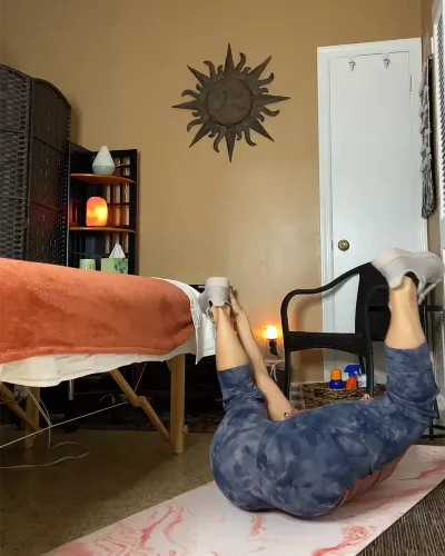 Author Marisa Savino lays on her back with her legs spread up in the air in happy baby yoga pose.