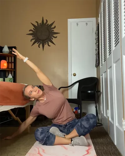 Author Marisa Savino performs a side-bend stretch yoga pose while seated on the floor.
