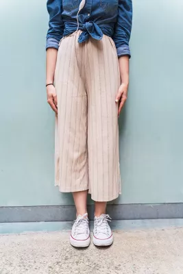 The bottom third of a woman is visible leaning against a wall, her feet are together, hands along her legs.