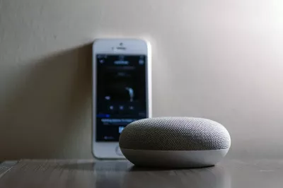 A cell phone and wireless speaker sit on a table.