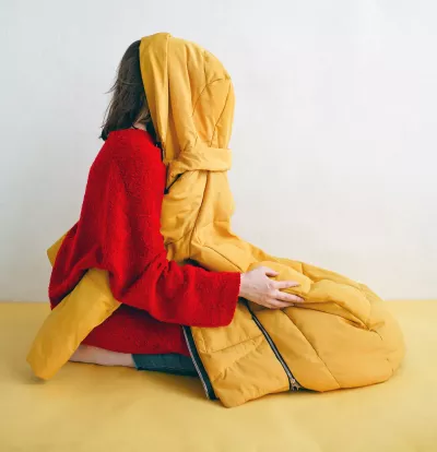 A woman kneels with a jacket covering her face.