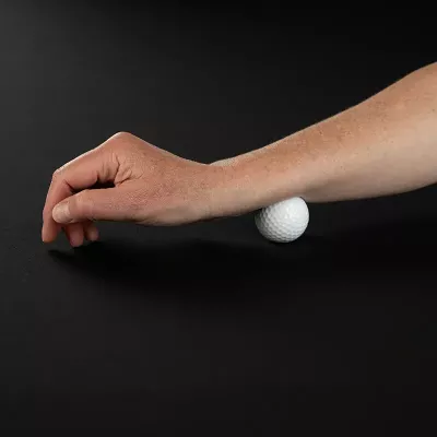 Demonstration of massaging the forearm with a golf ball on a table.