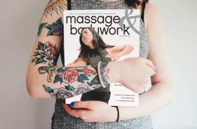 A woman with tattoos on her arms holding a copy of Massage & Bodywork July/August 2023.