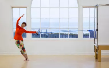 Judith Aston in a red top stretches in a dancing motion.