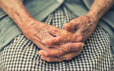 elderly woman sitting with hands folded in lap.