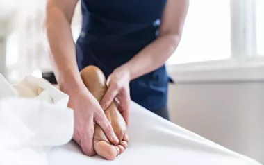 Massage therapist massaging bottom of client's foot.