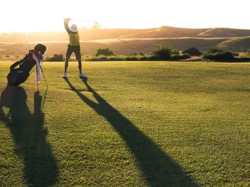 A golfer starts his backswing as the sun sets behind him.