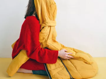 Woman kneels with jacket covering her face.