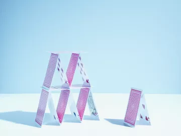 A tall tower of multiple playing cards stands next to a smaller tower of two playing cards.