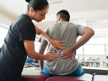 A female therapist does an assessment on a male client's back.