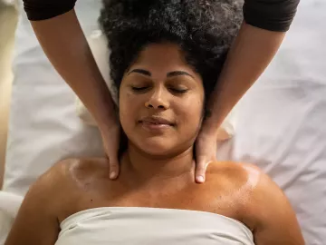 Massage therapist applying massage strokes to female client on massage table.