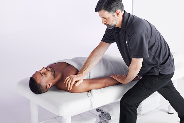 Male massage therapist performing massage on a prone client.