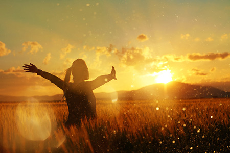 Woman in field at sunset with arms outstretched