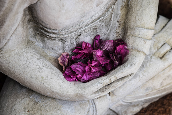 Stone Buddha statue holding dried flowers in its lap