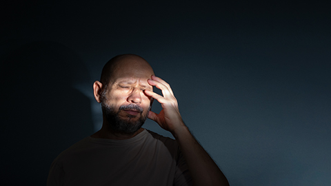 A person holding their head in pain in a dark room.