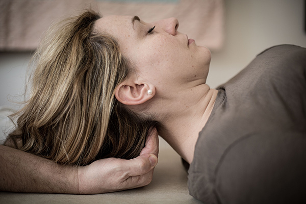 A woman lying on her back receiving craniosacral therapy