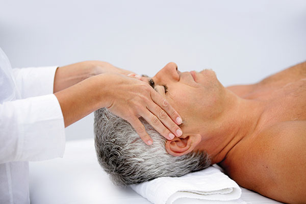 An older man receiving head massage while lying on a massage table