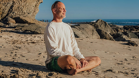 A man sitting on the beach with his legs crossed and eyes closed.
