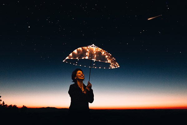 A smiling massage therapist holding a clear plastic umbrella as a shooting star passes above her