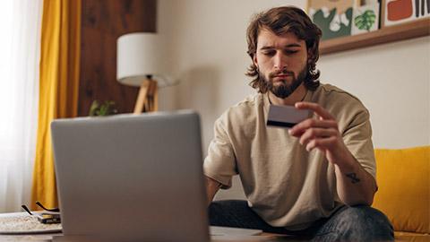 Image of a person sitting with a laptop looking at their credit card.