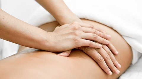Massage therapist using both palms to massage a clientâ€™s lower back.