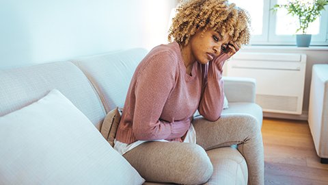 A woman sitting on the couch clutching her abdomen, thinking about pain.