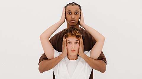 A pair of people with arms intertwined covering each otherâ€™s ears.